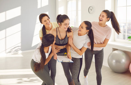 Happy smiling women group rejoicing the success in fitness after sport training standing in gym with...