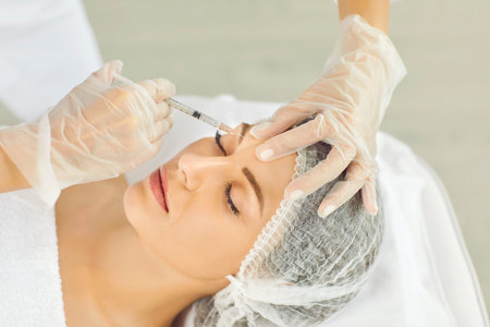 Hands of cosmetologist in gloves making rejuvenation anti wrinkle injection in beautiful woman face skin in a beauty spa salon. Cosmetic procedure, aesthetic cosmetology and facial treatment concept.の写真素材