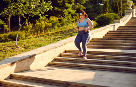Young overweight woman jogging on park staircase. Motivated fat large plump over weight stout lady...