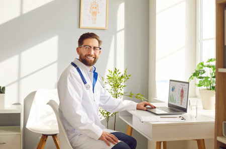 Male doctor portrait smiling medical assistant working laptop, wearing glasses, consulting online. Man performing medical job, consultant, healthcare administration, clinic management in public healthの写真素材