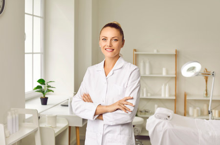 Portrait of a happy young smiling woman cosmetologist or beautician doctor standing in beauty spa salon office on her workplace and looking cheerful at camera. Cosmetology and skincare concept.の写真素材