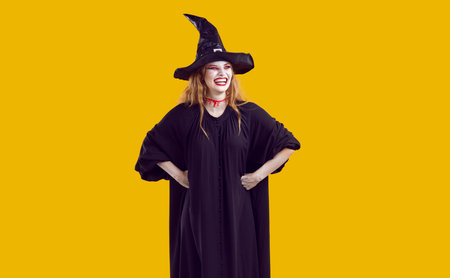 Laughing cheerful positive blondy woman in black witch costume and hat with scary mad make-up on...
