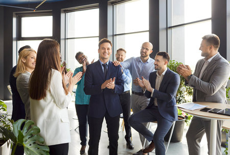 Friendly happy diverse employees congratulating businessman with great business achievement, good work results or job promotion, business people applauding friend and hr cheering in modern officeの写真素材