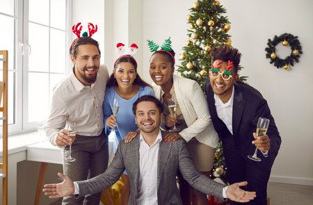 Portrait of cheerful young multiracial people posing together during New Year party. Men and women wearing Christmas accessories and holding glasses of champagne are smiling at camera at home party.の写真素材