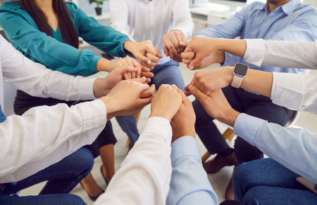 Close up shot of a diverse business people team holding hands in stack, sitting together in a...