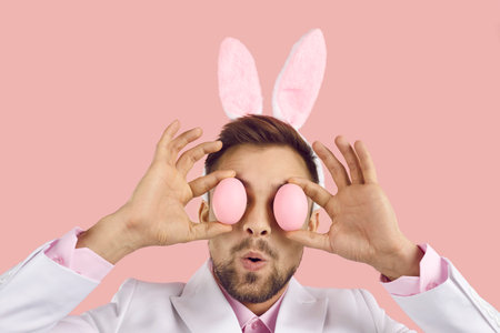 Closeup studio head shot of young man wearing white suit and cute plush toy bunny ears covering his...