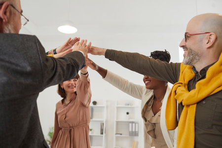 Diverse team of happy smiling confident multiethnic employees joining their hands as they gather...