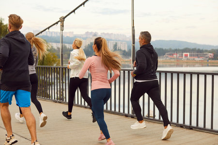 Backside view of a team of athletes running or jogging together in a city park. The group of people athletes is dedicated and focused, enjoying their run or jog in the urban nature.の写真素材