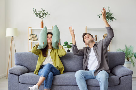 Annoyed couple at home, covering ears with pillow, unhappy irritated family trying ignoring loud noise sound, feeling stressed of noisy disturbing neighbors, loud music, hating hearing sound of worksの写真素材