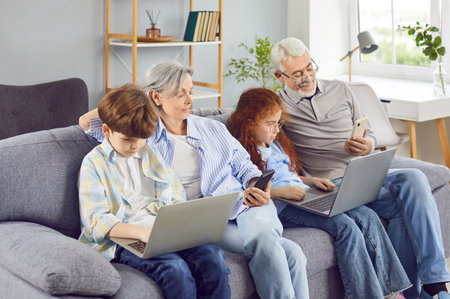 Happy grandparents with grandchildren girl and boy sitting on sofa using modern laptop and...