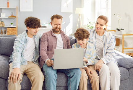 Happy family with teen and little kid sons sitting on sofa to have fun using modern new laptop...