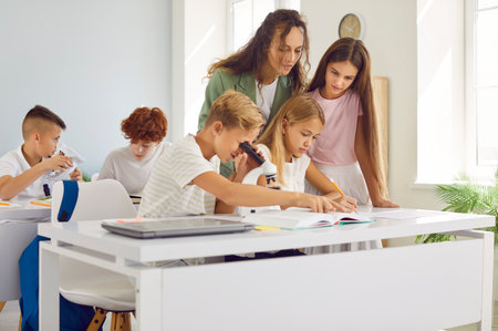 Teacher assisting students during a lesson in a school classroom. Working together as a group, showing teamwork and collaboration between teacher and pupils. Creating supportive learning environment.の写真素材
