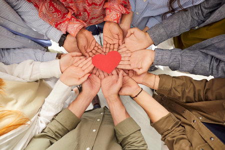Top view of multiethnic people hands holding red paper heart symbol. Group of people standing in circle, promoting unity, love and support for World Organ Donation Day. Charity and altruism concept.の写真素材