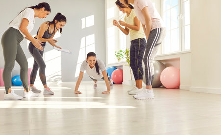 Group beautiful sportswomen applaud a girl standing on the floor in a plank in the gym. The concept...