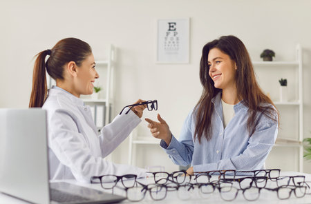 Ophthalmologist helping finding right pair of glasses, perfect correct optical frame, to client,...