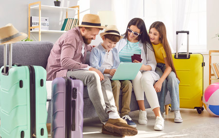 Family mom dad son and daughter sit on sofa browsing laptop booking hotel for their trip bags ready for family vacation. Essence of family vacation sharing excitement of planning togetherの写真素材