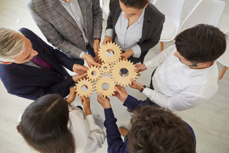 Team of business people connect cogwheels as metaphor for good teamwork and work efficiency, high angle, from above. Senior and young entrepreneurs form an alliance and organize parts into one systemの写真素材