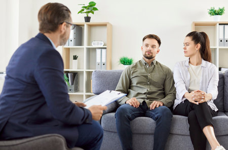 Young couple talking about marriage problems sitting at family therapist office during therapy session. Male psychologist listening his patients trying to find solution. Mental health conceptの写真素材