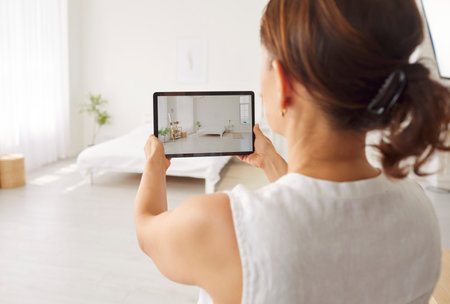 Portrait of a young woman house seller taking photo or making video on modern tablet of bedroom home interior. Rental agent or female realtor planning to sell apartment. Real estate concept.の写真素材