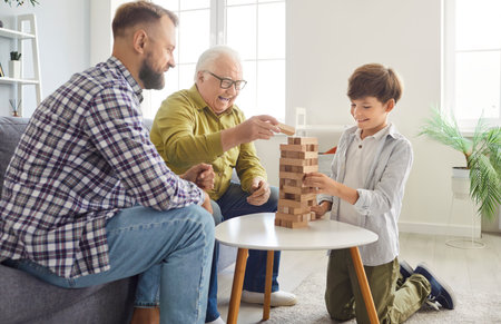 Father, son, and grandfather enjoy leisure time playing a game together at home. They laughing and bonding as a family, celebrating Father Day with joy and fun in a relaxed atmosphere.の写真素材