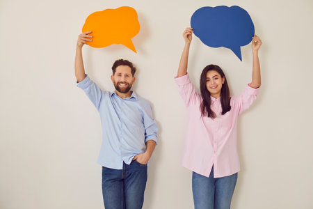 Portrait of a confident smiling couple holding empty colorful speech bubbles above their heads...