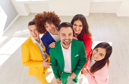 Group portrait of young people in colorful business suits standing in a circle and smiling at the camera. The happy and colorful crowd reflects teamwork and unity in a business environment.の写真素材