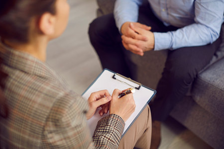 Woman therapist with a clipboard and a sheet of paper talking to a male patient during a psychotherapy session. Therapy, stress, mental health problems concept backgroundの写真素材