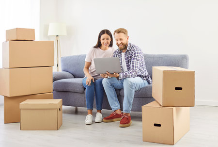Married couple enjoying time together while relocating to a new home. Use a laptop during the moving...