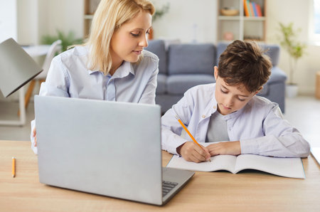 Young little schoolboy sitting at the desk at home and doing his homework with mother. Child boy...