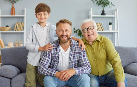 Portrait of a happy grandfather, father, and son smile, sitting on sofa at home, celebrating Father...