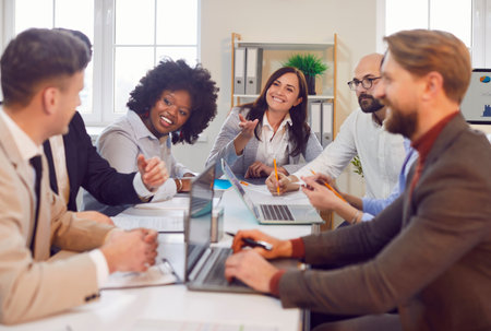 Diverse joyful confident people sitting at table in meeting room having business conference in modern office. Company employees discussing new projects at working place. Teamwork concept.の写真素材