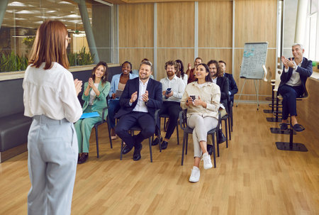 Happy audience applauding woman speaker after her presentation at business meeting or seminar. Group...