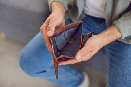 Close up top view of poor unrecognizable unemployed man wearing casual clothes holding opening empty wallet sitting on sofa at home. Bankrupt, no money, financial crisis and cost control conceptの写真素材