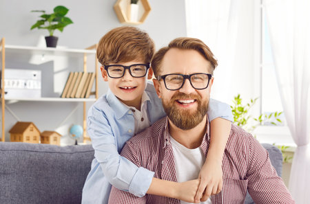 Positive portrait of a young happy Caucasian son embracing his delighted father at home, both smiling and laughing, looking at camera, capturing a joyful family moment for fathers day.の写真素材