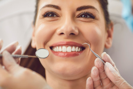 Happy female patient visits a dentist doctor who checks teeth using dental instruments in the clinic office. This oral care and therapy ensure the patient dental health and well being.の写真素材