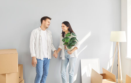 Cheerful family couple standing with flower between cardboard boxes in their new home on moving day....