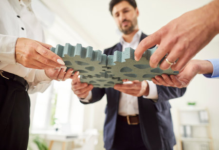 Cropped image of three business team people holding gear wheels in their hands, putting it together. Company workers join plastic gears in office. Partnership, teamwork and finding working solutions.の写真素材