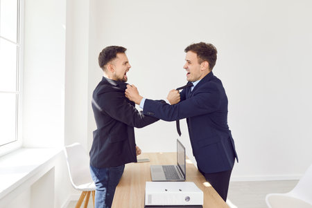 Angry business people colleagues disputing having disagreement fighting at workplace. Aggressive coworkers arguing having conflict standing at desk in office. Business conflict concept.の写真素材