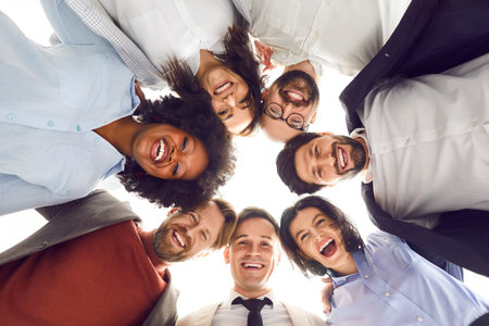 Bottom view group portrait of a happy multinational business team smiling and looking at the camera together in the office, standing in circle. Happiness and teamwork in diverse office environment.の写真素材