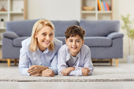 Portrait of a happy mother and son lying on the floor at home, looking affectionately at the camera. Strong family bond and relationship highlight the love between parent and child.の写真素材