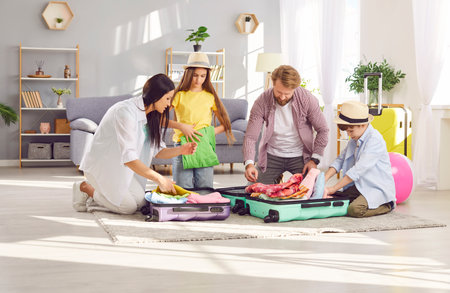 Young family of four with two kids boy and girl packing suitcases preparing for summer vacation trip sitting on floor at home together. Travelling, holiday tour and journey concept.の写真素材