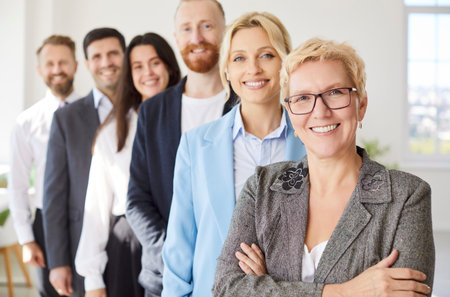 Group of business confident people men and women looking cheerful at camera and smiling indoors. Employees in formal clothes standing in office in a row. Team work concept.の写真素材