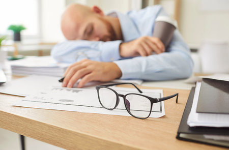 Tired sleeping office man, employee falling asleep at desk overworked, exhausted sleeps stressed male manager lying on table and sleeping after hard working day, no energy left, glasses put awayの写真素材