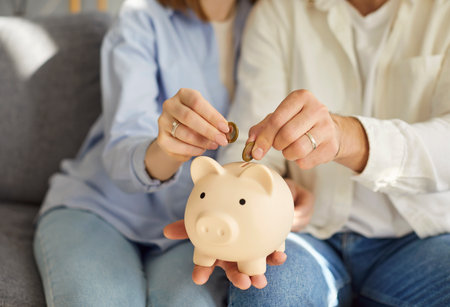 Cropped shot of young family couple sitting on sofa, holding piggy bank, planning their budget...