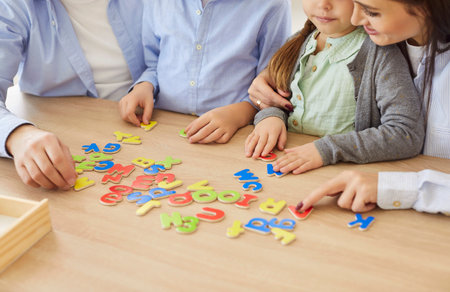 Close up of young family playing with colorful alphabet letters on table. Parents and children...