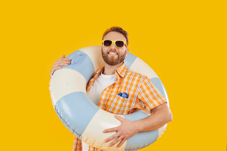 Summer ready. Portrait of cheerful man holding large blue and white inflatable lifebuoy on yellow...