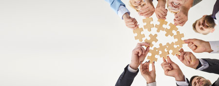 Bottom view of confident business people putting together pieces of wooden puzzles. Colleagues join...