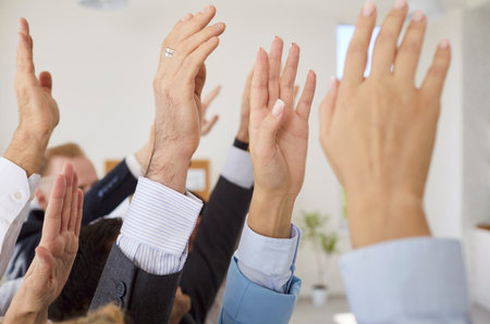 Closeup of business people hands raising hands to vote at the conference standing in meeting room. Company employees in formal clothes men and women voting in office during a meetingの写真素材