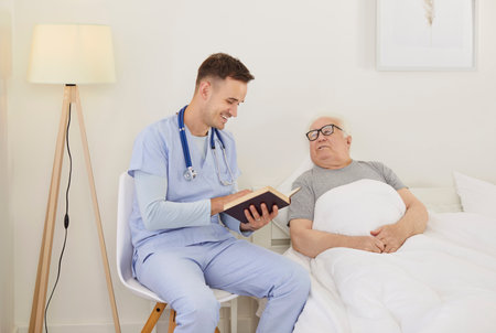 Caregiver or doctor reading a book to an senior man patient in a nursing home before bedtime, enhancing the leisure experience. A warm and supportive moment encourages relaxation and companionship.の写真素材