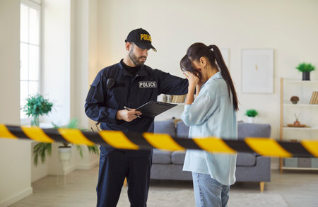 Portrait of a young woman crime victim covering face with hands standing with policeman putting his hand on her shoulder to support her. Crime, robbery and domestic violence concept.の写真素材